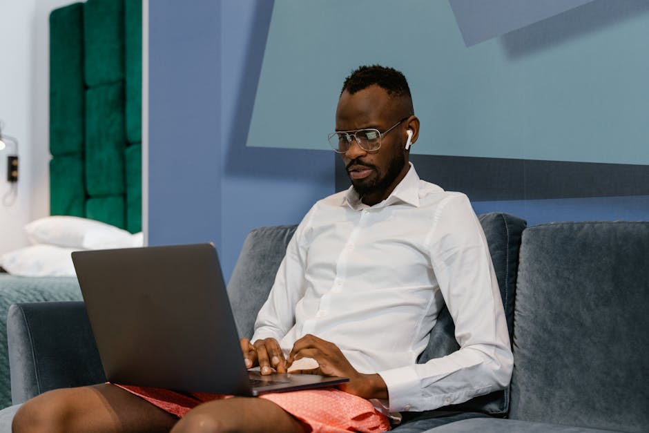 A man in casual attire focuses on his laptop in a modern home setting.